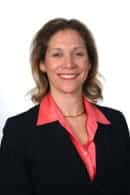 .Portrait of a professional woman smiling confidently in a business suit with a pink blouse, representing a confident speaker who could benefit from Accent Reduction Classes